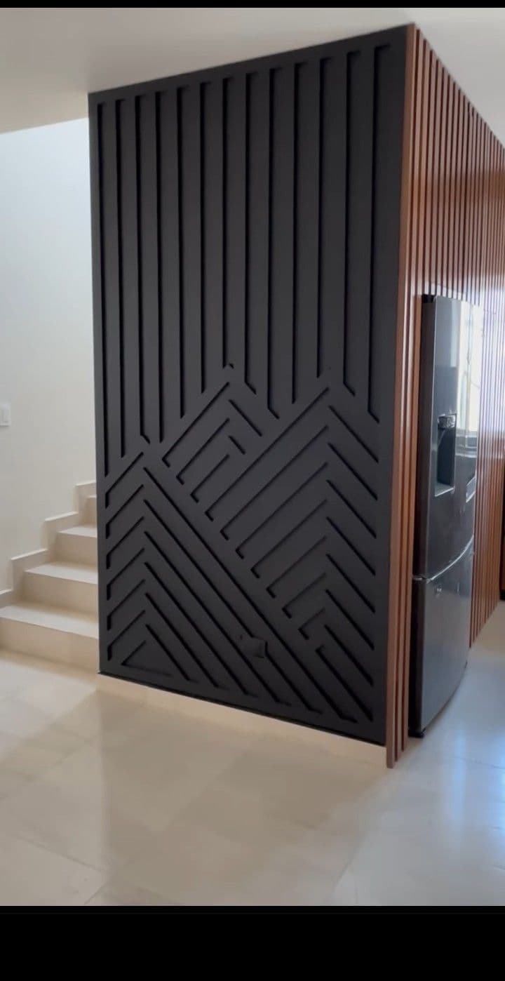 Black slatted accent wall with abstract geometric cutouts and natural wood panels, showcasing custom wallpaper installations.