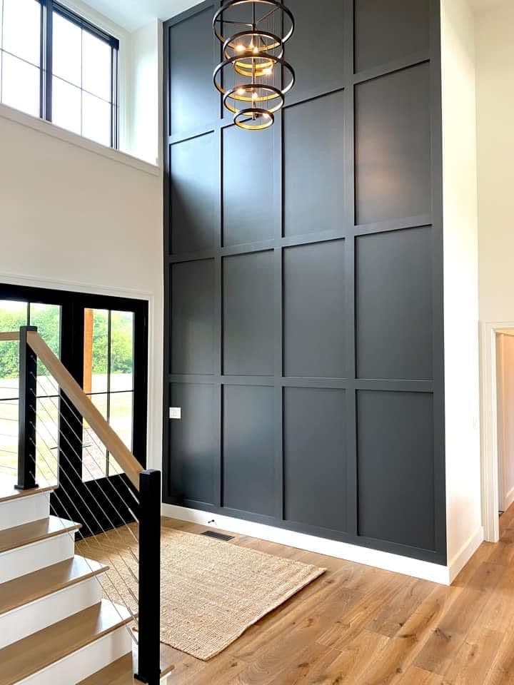 Tall dark accent wall in a modern entryway with high ceilings and staircase.
