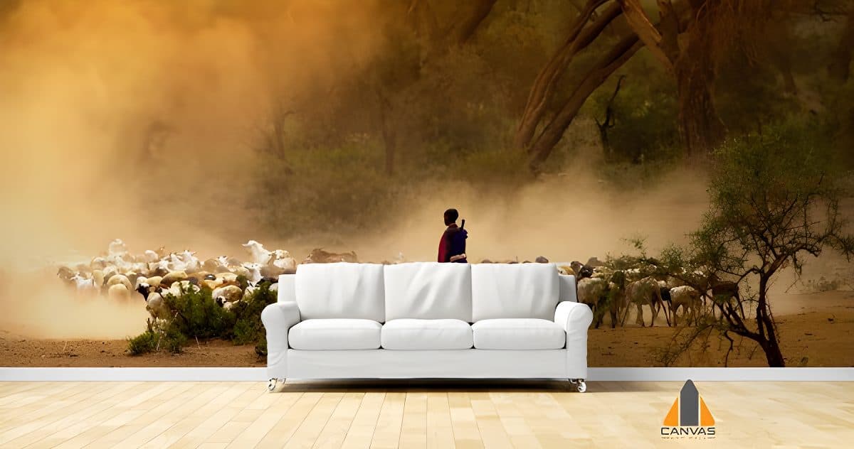Shepherd leading goats through dusty landscape wall mural in a modern living room with white couch.
