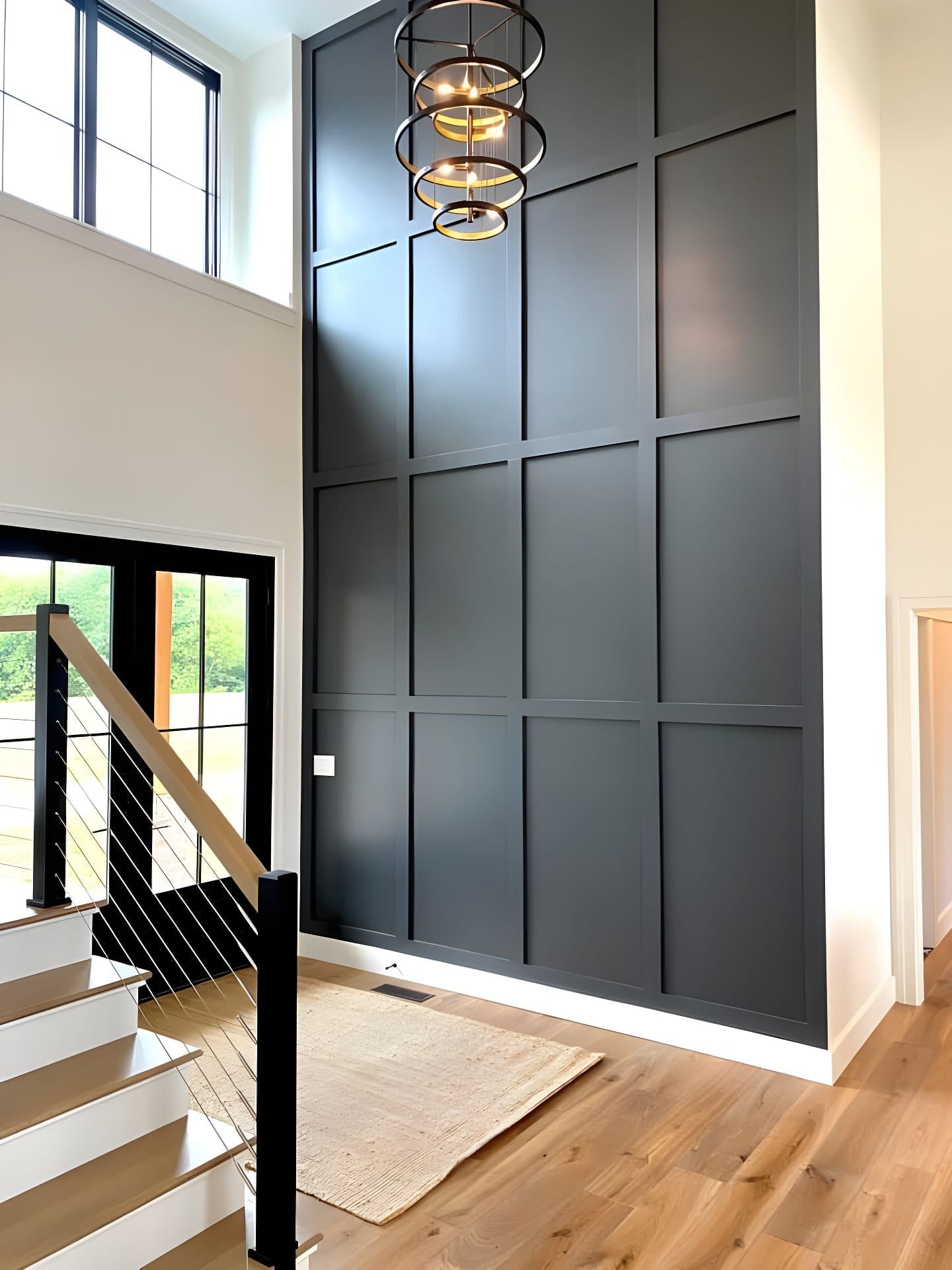Tall dark accent wall in a modern entryway with high ceilings and staircase.