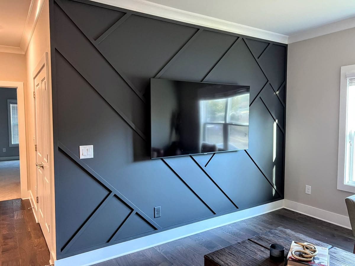 Dark gray accent paneling on a living room wall with a mounted TV, showcasing a custom wallpaper installation.