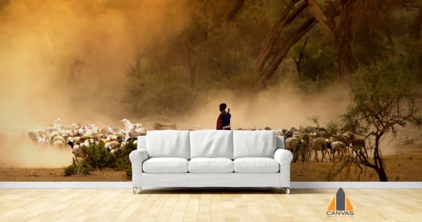 Shepherd leading goats through dusty landscape wall mural in a modern living room with white couch.
